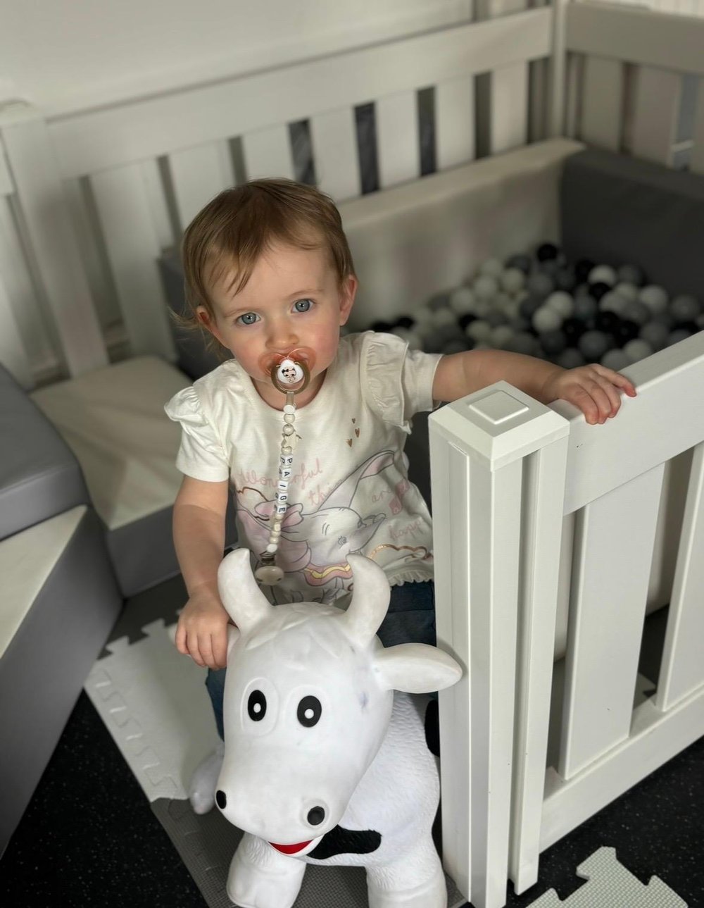 Toddler on a white cow hopper inside the soft play ball pit surround