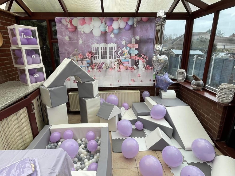 First birthday soft play with Alice in Wonderland backdrop and lilac balloons