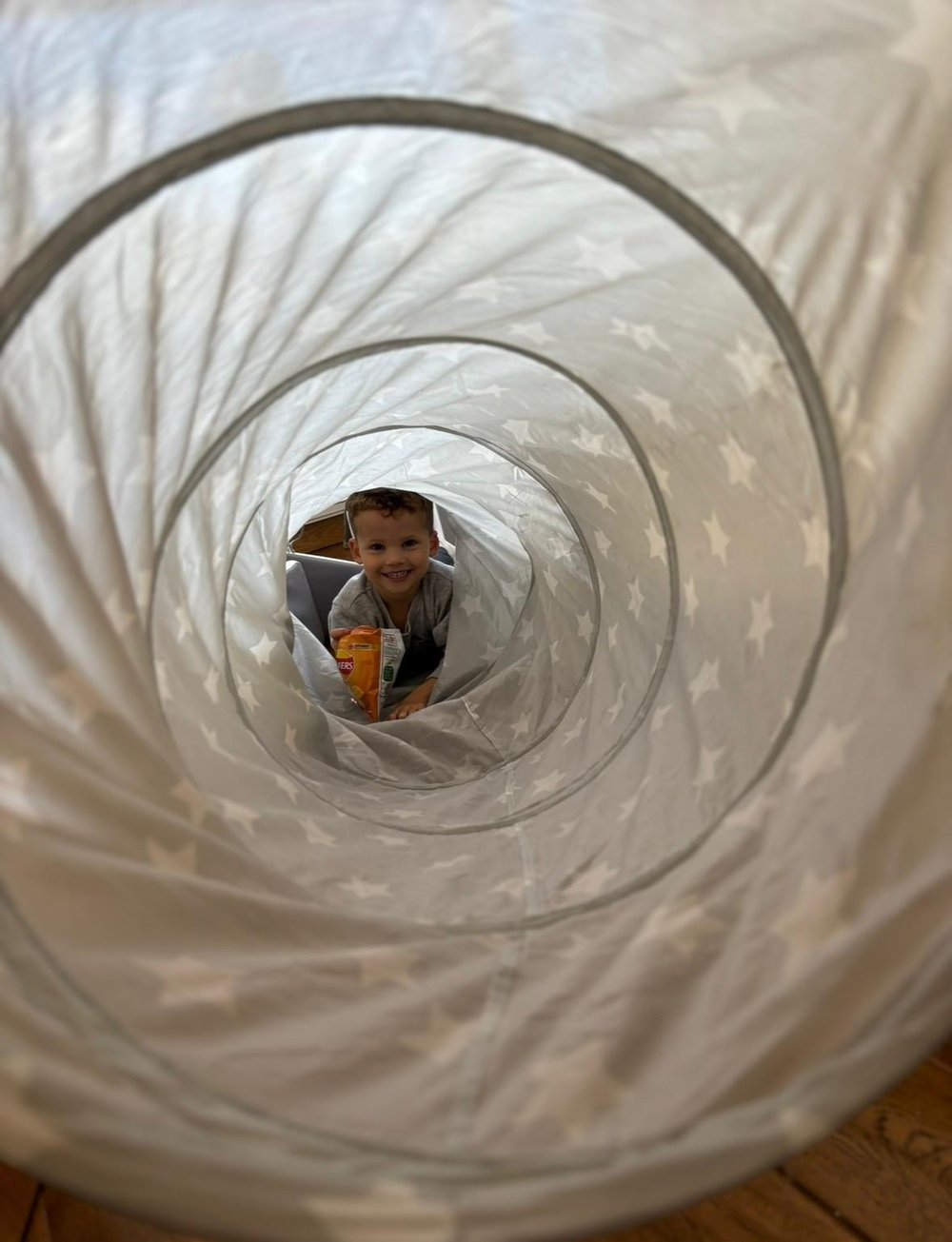 Little boy smiling through the star-print soft play tunnel
