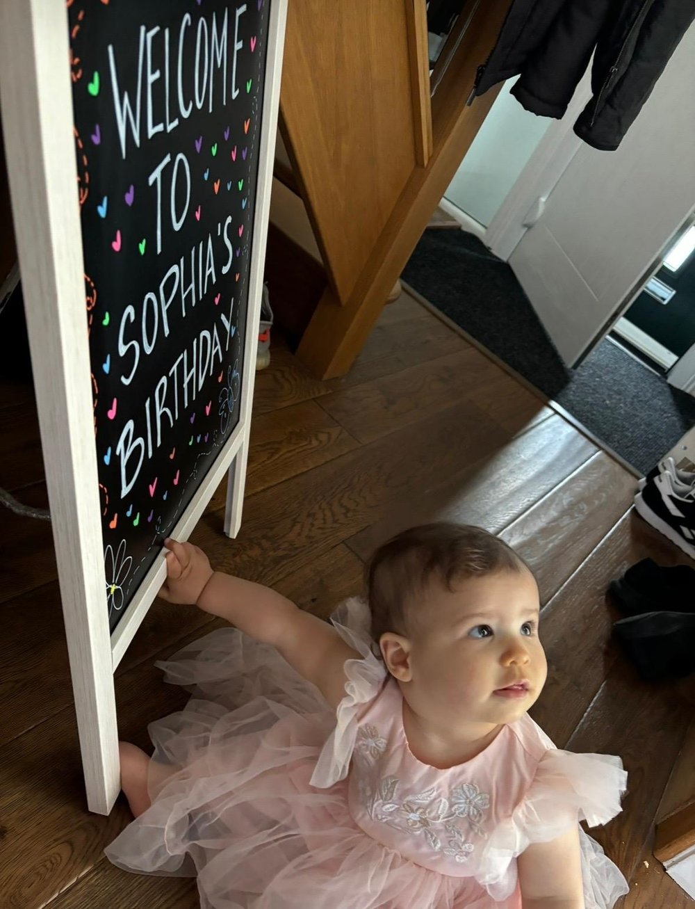 Little girl in a pink tutu next to a welcome to Sophia's birthday chalkboard